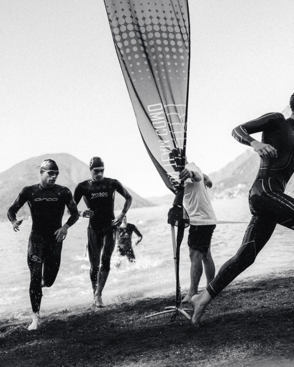 Triatleten in wetsuits lopen het water uit bij de swim-exit, zwart-wit